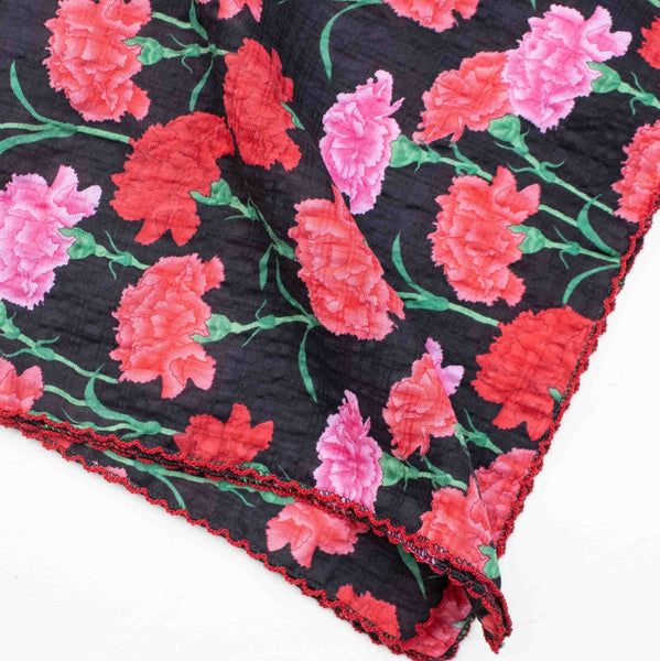 cotton blend seersucker square scarf in black background and pink & red carnation flower pattern with red scalloped embroidered trim. Shown folded in close up