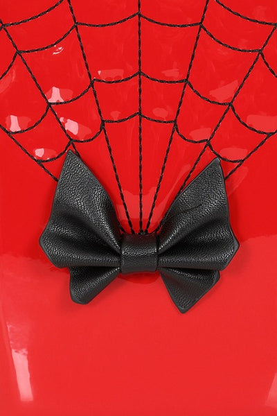 Cherry red patent vinyl handbag in the shape of a scalloped coffin with a black bow detail, hand strap, and black spiderweb patterned stitching. Shown from front in close up of bow and stitching detail