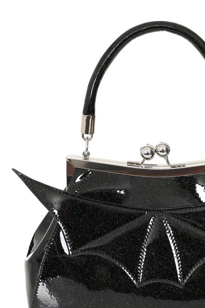 A black patent vinyl with shimmery silver handbag with a glossy finish, featuring a bat-wing design on the front, a top handle, and a silver-tone kiss-lock clasp. Shown from front in close up of batwing detail