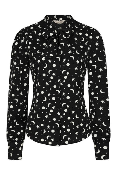 a matte finish satin long sleeve button down blouse in a black background scattered white star, crescent moon, and full moon allover pattern with a tie neck collar, slightly puffed shoulders, and button cuffed sleeves. Shown from front