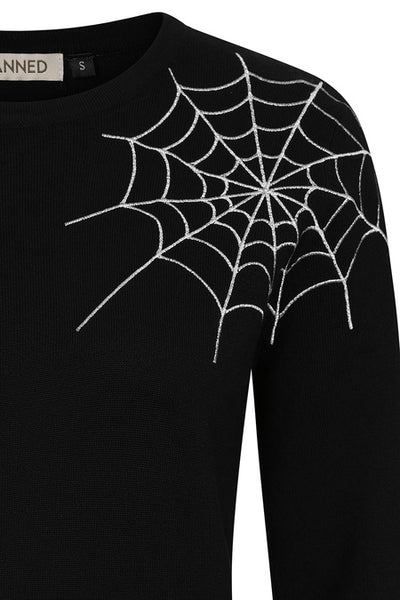 black crewneck knit sweater with ribbed neckline, bottom band, and cuffs with bright white embroidered spiderweb detail at left shoulder extending to neckline. Shown from front in close up of embroidery detail