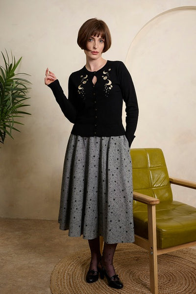 model wearing black cardigan and grey tweed high waisted swing skirt with all over flocked black star pattern, fabric covered button detail at waistband, and pockets. Shown from front