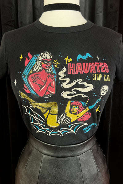 cropped black t-shirt with printed illustration of two cartoon women, one standing in a coffin wearing a mask and the other lying in a spiderweb holding a skull with the caption "THE HAUNTED STRIP CLUB" "WEIRDOS ONLY". Shown on close up on dress form