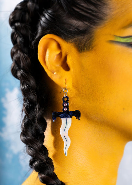 pair of acetate dangle earrings in the shape of small daggers with wavy iridescent blades and marbled blue and white handles with a row of three rhinestones in each. Shown worn on model from side