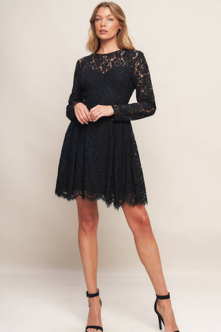 model wearing a black lace mini dress with long sleeves, round neckline with sweetheart style bodice lining, reverse yoke waistband with scalloped hem ending above the knee. Shown from front