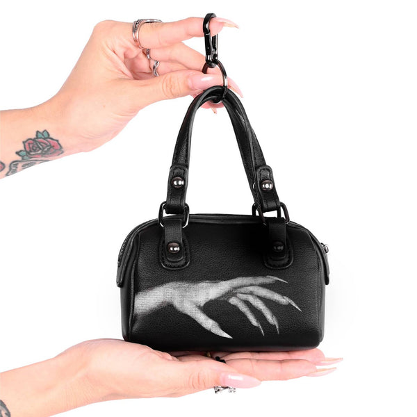 Black faux leather mini purse shaped bag charm with white printed design of vampiric hand with long nails. Bag has gunmetal hardware, zip closure, and split ring keychain with clasp. Shown from front held to show scale
