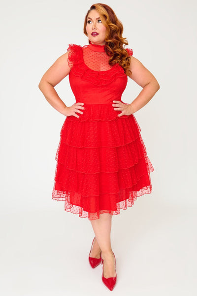 A plus size woman modeling a bright red heart-patterned lace dress with high banded neckline, ruffled yoke bodice, and just below the knee five tiered matching lace skirt. Shown from front.