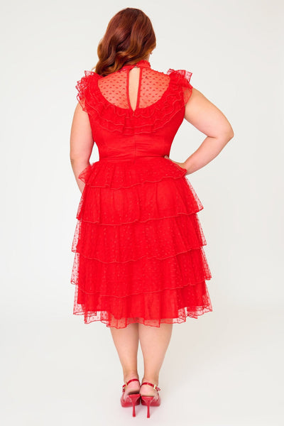 A plus size woman modeling a bright red heart-patterned lace dress with high banded neckline, ruffled yoke bodice, and just below the knee five tiered matching lace skirt. Shown from back