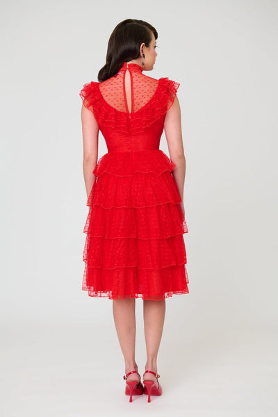 A woman modeling a bright red heart-patterned lace dress with high banded neckline, ruffled yoke bodice, and just below the knee five tiered matching lace skirt. Shown from back