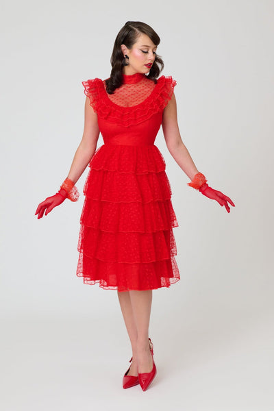 A woman modeling a bright red heart-patterned lace dress with high banded neckline, ruffled yoke bodice, and just below the knee five tiered matching lace skirt. Shown from front.