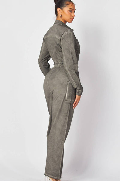 model wearing denim boilersuit in grey mineral wash finish. Boilersuit has long sleeves, pointed collar, silver metal zip down the center, elasticized waist with belt loops, large hip pockets and chest pockets, and full length legs. Shown from back