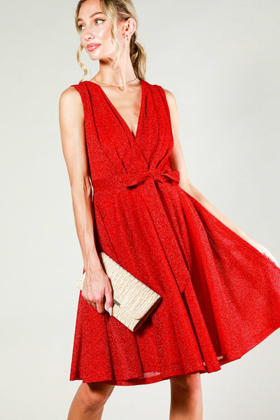 bright red lurex sleeveless dress featuring pleated surplice v-neck bodice, banded waist with removable matching sash belt, and a swing-y full circle just-above-the-knee length skirt. shown on a model.