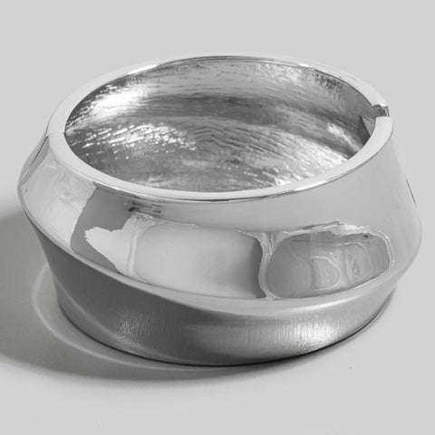 Silver metal hinged bangle with an asymmetrical diagonal pinched curved design. Shown flat