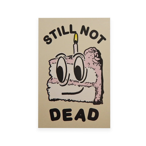 rectangular heavyweight note card with image of smiling cartoon slice of cake with single candle and message "STILL NOT DEAD" in black