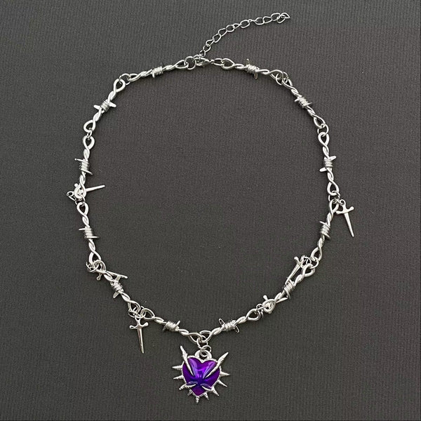 Silver necklace with barbed wire style chain, dangling tiny dagger pendants, and purple enameled spiked heart pendant on a dark background