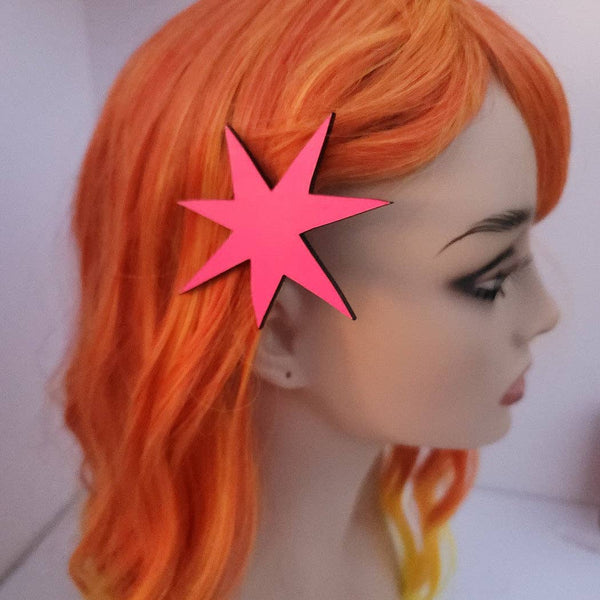 asymmetrical starburst hair clip made of UV reactive neon pink acrylic shown on mannequin head with bright orange wig
