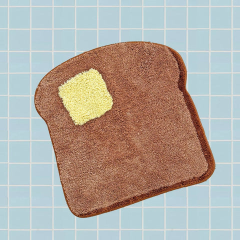 soft pile rug in the shape of a brown piece of toast with square piece of butter in the corner. Shown on blue tile background