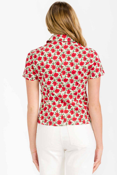 model wearing cotton short sleeve blouse with warm off-white background pattern of red and black flowers with green leaves. Has a notched collar and matching red plastic buttons. Shown from back