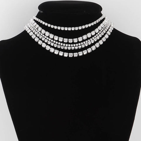 Silver metal necklace with multiple strands of varying sizes of square rhinestones on a black mannequin bust against a white background