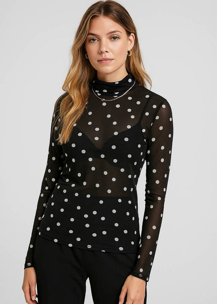 model wearing a black mesh turtleneck top with an allover print of white polka dots. Shown from front