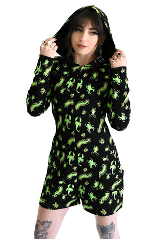 model wearing a black long sleeve hooded onesie with neon green insect pattern, front zip closure, and mid-length shorts. Shown from front with hood up