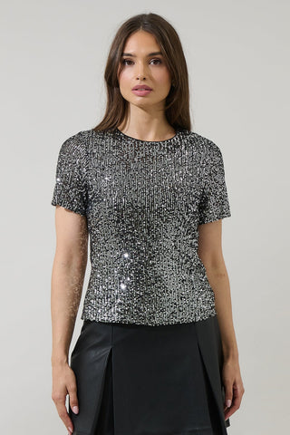 model wearing black short sleeve top with round neckline, black background and allover silver sequin adornment. Shown from front