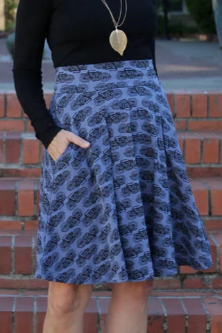 stretch cotton knit high-waisted just-above-the-knee length flared skirt in a slate blue background with repeat black vintage motorbike pattern. shown worn by a model