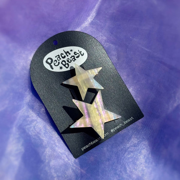 Pair of two different sized asymmetrical star-shaped acetate hair clips with iridescent striped pattern. Shown on black backing card