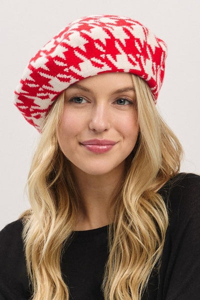 Woman wearing a red and white houndstooth patterned knit beret against a plain background