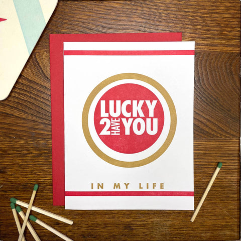 rectangular letterpress heavy cardstock greeting card meant to resemble design of Lucky Strike Cigarettes pack with message "LUCKY 2 HAVE YOU IN MY LIFE" in gold and white