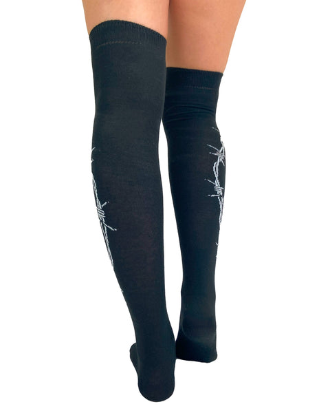 over-the-knee length socks in solid black cotton with white knit in pattern of barbed wire running down the outer leg of each sock, shown on model from back