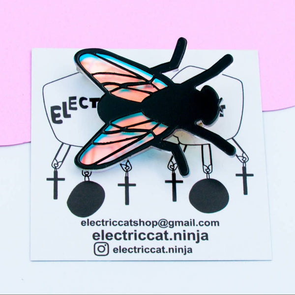 layered acrylic brooch of a black fly with iridescent translucent blue wings. Shown on backing card