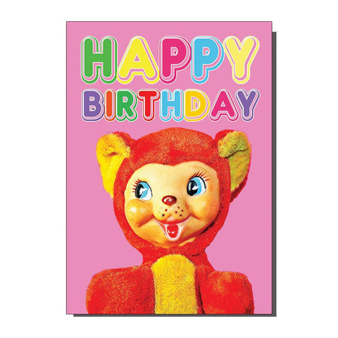 Rectangular note card with “HAPPY BIRTHDAY” written in multicolored bubble letters on a pink background above a photograph of an old stuffed bear made of yellow and red faux fur with a plastic face