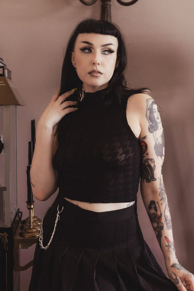 model wearing a black sheer mock neck sleeveless crop top with a ribbed base pattern and all over large houndstooth print. Shown from front