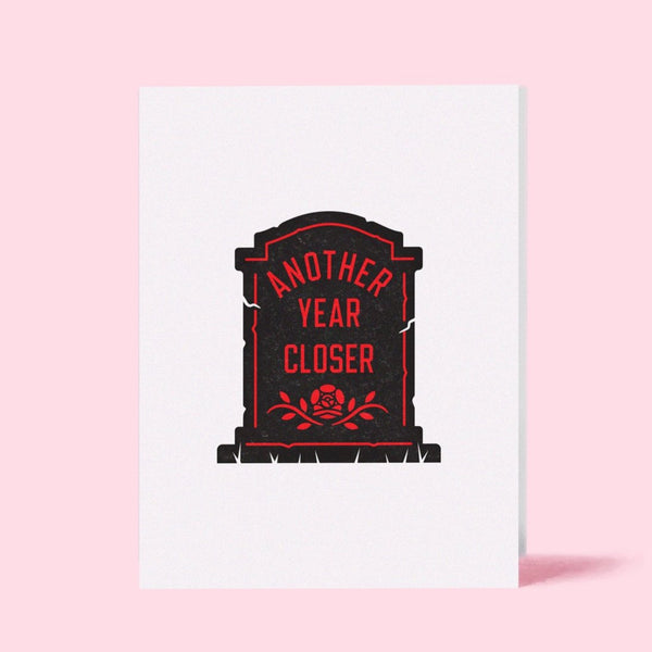 white rectangular letterpress greeting card with black and red image of a gravestone with inscription "ANOTHER YEAR CLOSER"