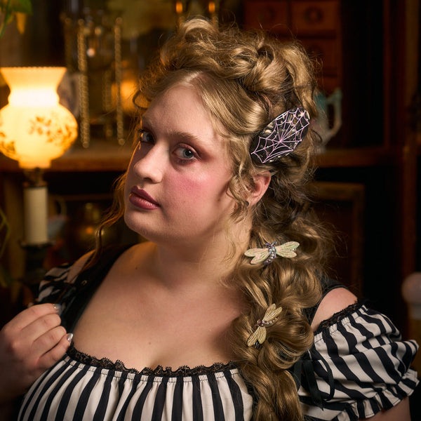 black oval hair claw clip made of marbled black plant-based cellulose with a pink spiderweb design and small silver rhinestones shown worn by woman with long curly hair