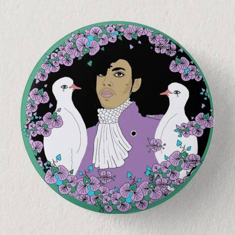 pinback button of Prince alongside two crying white doves on black background with purple and green floral border