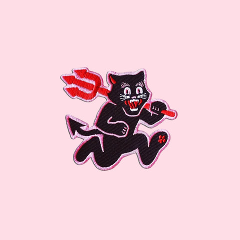 an embroidered patch of a black cat running on its hind legs holding a red pitchfork with its mouth open