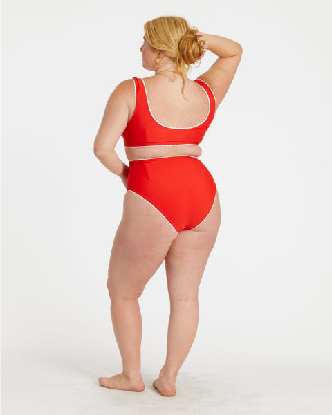 model wearing red and white gingham print reversible bikini. Top has scoop neckline and white rickrack style trim. Shown from back with solid red side worn