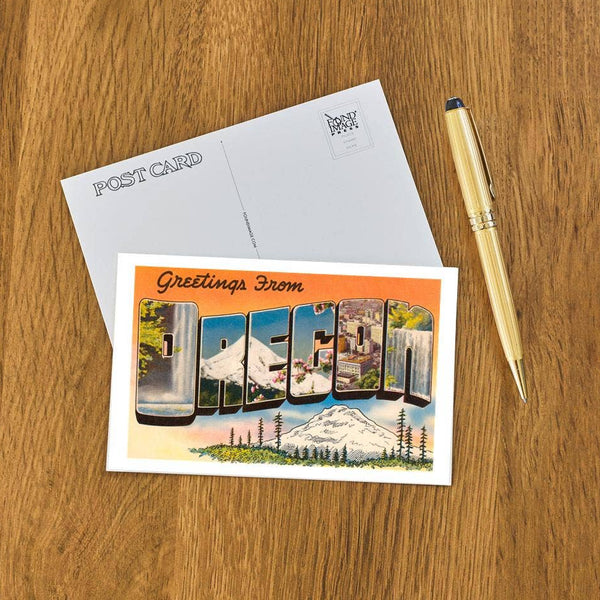 Vintage-style 'Greetings from Oregon' postcard with scenic elements and a pen on a wooden surface
