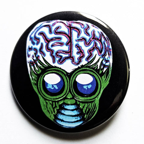 1.25 round pinback button with a stylized alien mask design in green, pink, blue, and white on a black background