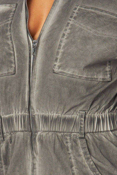 model wearing denim boilersuit in grey mineral wash finish. Boilersuit has long sleeves, pointed collar, silver metal zip down the center, elasticized waist with belt loops, large hip pockets and chest pockets, and full length legs. Shown from front in close up of chest for fabric detail