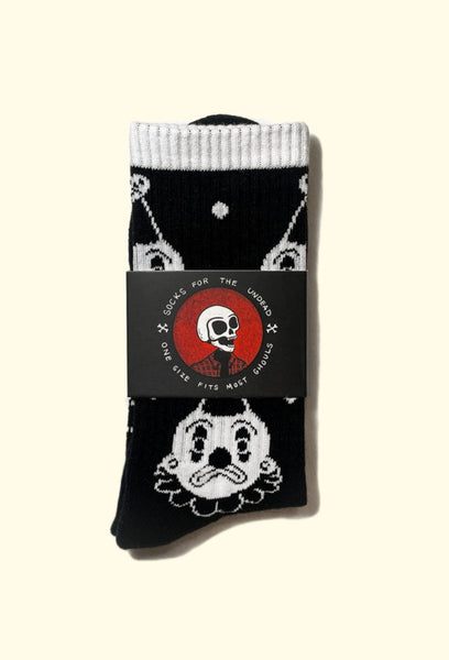 black cotton crew socks with white cuffs and an all over pattern of a white and black clown with either a smiling or frowning face. Shown flat in packaging