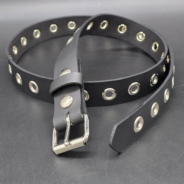 A black leather belt with a row of silver metal grommets running the length of the belt, coiled on a dark gray textured surface shown with buckle