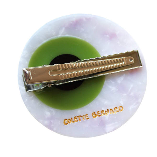 eyeball shaped hair clip with a white marbled white, red carved bloodshot details, a bright light green iris, and a black pupil in the center, on a white background. Shown from back, displaying silver metal alligator style clip and gold branding