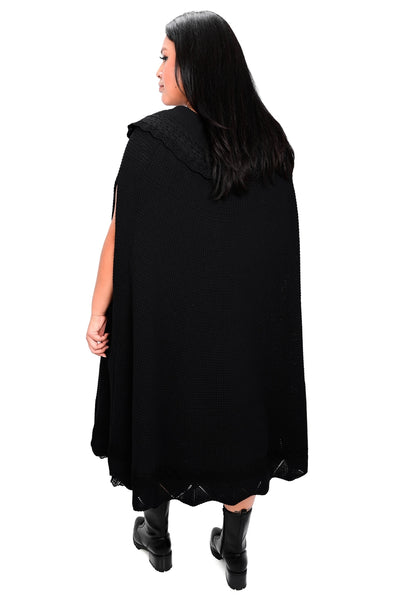 Model wearing black waffle sweater knit cape with scalloped collar and bottom hem with lace detail at collar and bottom hem and black drawstring with silver crescent moon charms. Shown from back