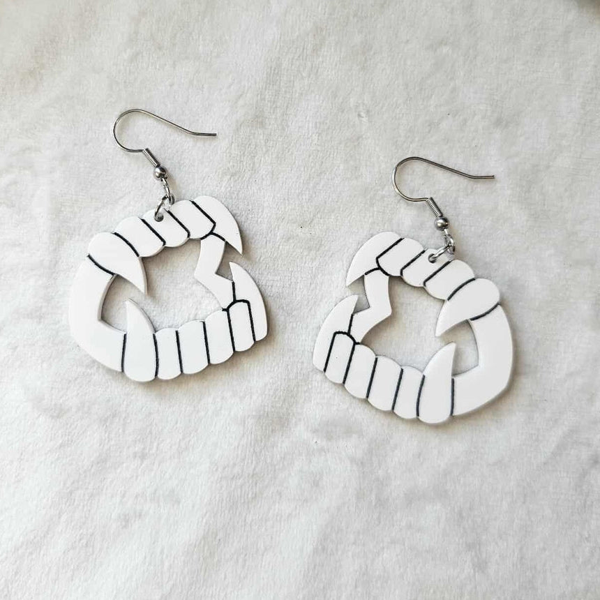 Pair of white laser-cut acrylic dangle earrings with black painted detail of a pair of novelty vampire teeth with fangs