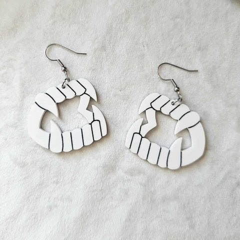 Pair of white laser-cut acrylic dangle earrings with black painted detail of a pair of novelty vampire teeth with fangs