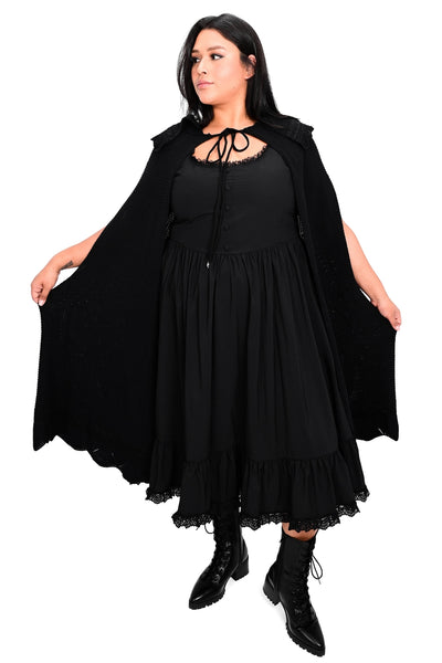 Model wearing black waffle sweater knit cape with scalloped collar and bottom hem with lace detail at collar and bottom hem and black drawstring with silver crescent moon charms. Shown from front