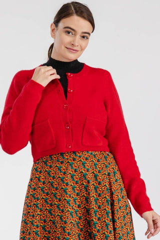 model wearing a long sleeved cropped bright red knit cardigan with slightly ballooned sleeves, patch pockets at the front of the sweater, red plastic buttons, and ribbed cuffs and hems. 